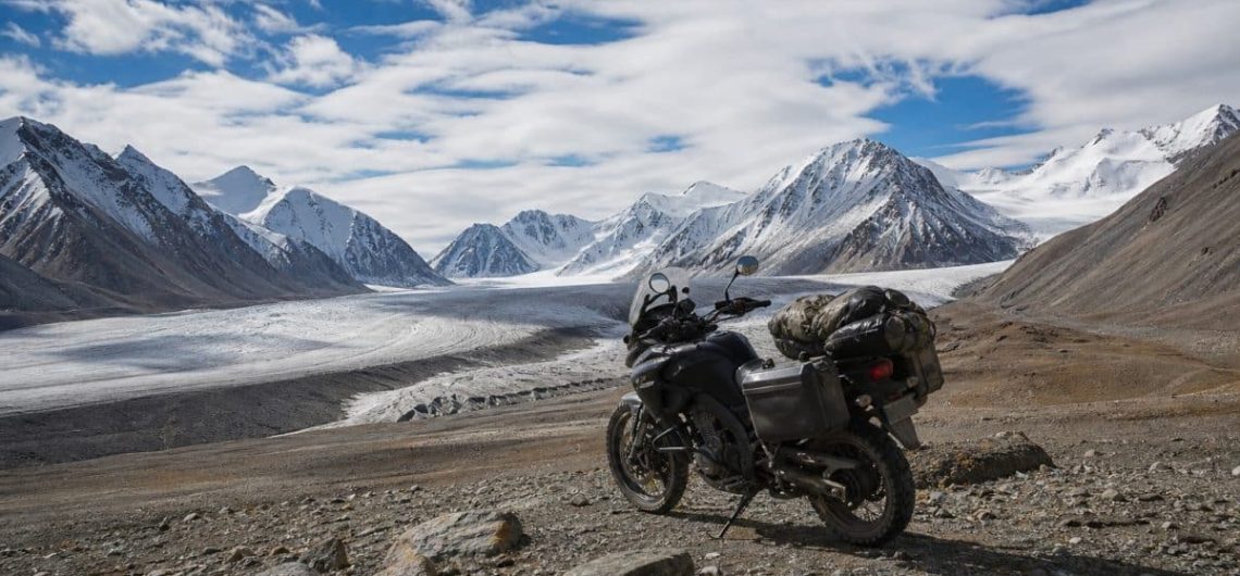 Loaded adventure motorcycle on moraine below a Mongolian glacier and snow peaks