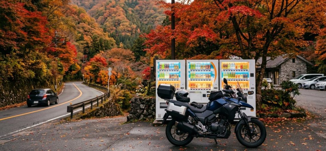 Touring motorcycle beside vending machines at a Japanese mountain rest stop in autumn