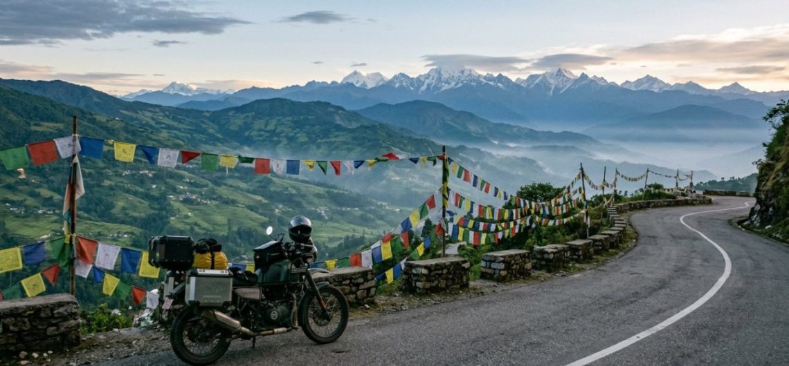 Touring motorcycle on a mountain road above the Kathmandu valley at dawn with prayer flags and Himalayan peaks